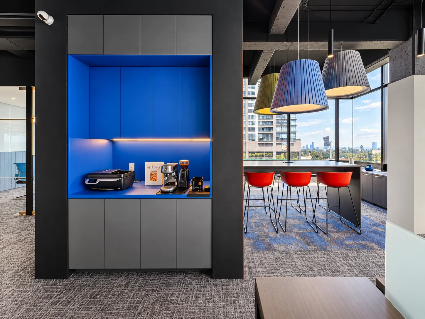 Kitchen area with a blue coffee niche, red stools and pendant lamps by the windows