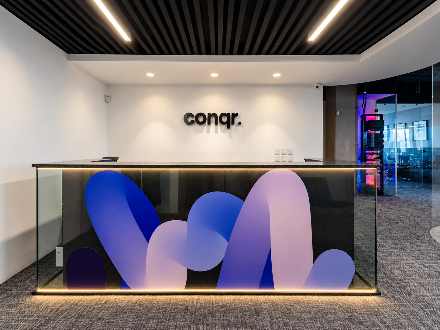 conqr. reception desk with the logo on a white wall and a blue and lilac graphic on the counter